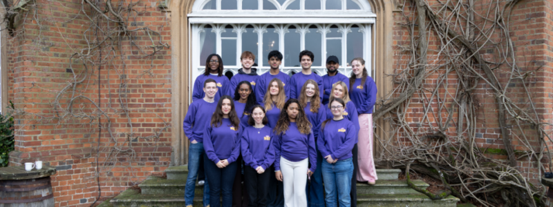 Smiling Youth Ambassadors wearing purple jumpers outside Cumberland Lodge